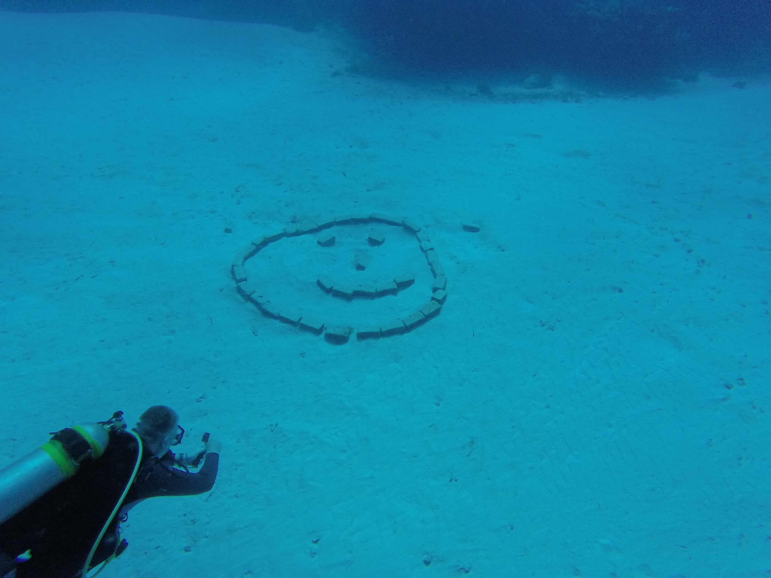 A scuba diver near a smiley face arranged on the sea floor
