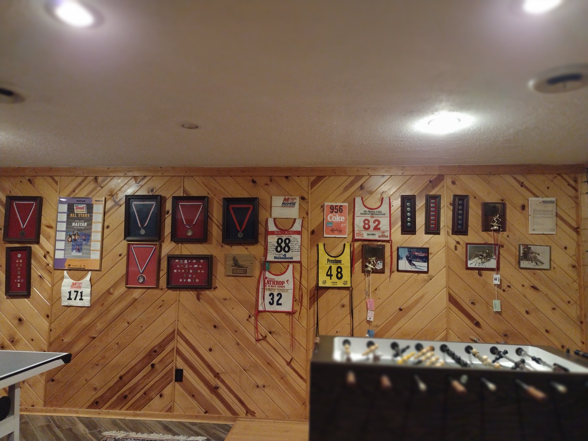 Wide view of Vince's skiing medals, race bibs, and awards displayed on a wall